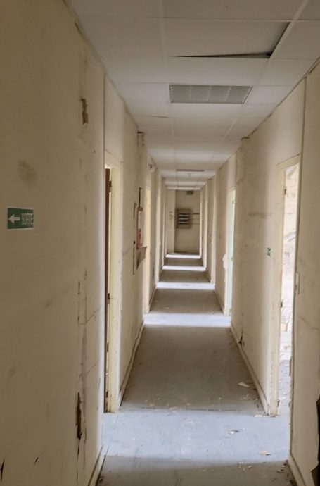 Couloir étroit avec plusieurs portes et murs jaunis, éclairage naturel.